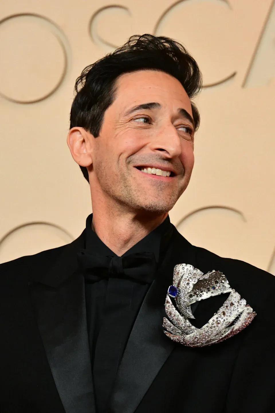 Adrien Brody wearing a massive brooch at the Oscars 2026 red carpet